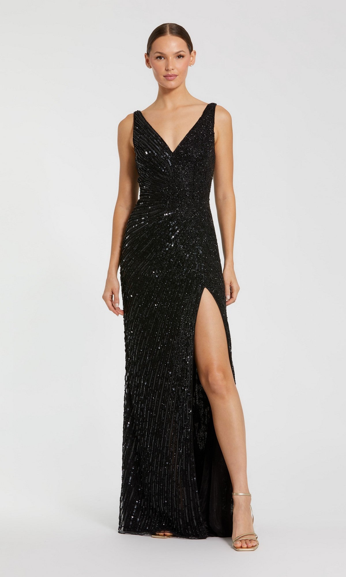 A woman wears the Sleeveless Beaded Formal Dress: Mac Duggal 5473, a black floor-length gown with sequins, a deep V-neck, high side slit, and sleeveless design, standing against a plain light background.