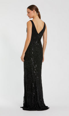 Woman in a sleeveless, beaded Mac Duggal 5473 formal dress with a fitted, floor-length black silhouette and deep V-back, stands against a plain white background facing away from the camera.