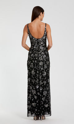A woman faces away, wearing the Mac Duggal 5477 Floral-Beaded Long Formal Dress—sleeveless, black with white floral beading—and silver high heels.