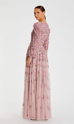 A woman stands facing backward, looking over her shoulder. She is wearing the Mac Duggal 5497—a modest, long-sleeve beaded formal dress in light pink with floral embroidery.