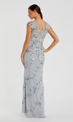 A woman faces away in the Mac Duggal 5500 Beaded Long Formal Dress, a light blue floor-length gown featuring cap sleeves, a V-shaped back, and shimmering beadwork against a plain light background.