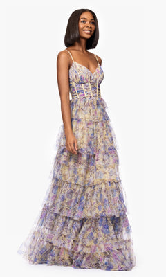 A woman stands against a white background wearing the Blondie Nites 5500BN Floral-Print Long Prom Dress, featuring a sleeveless design, fitted bodice, spaghetti straps, and floor-length floral print.