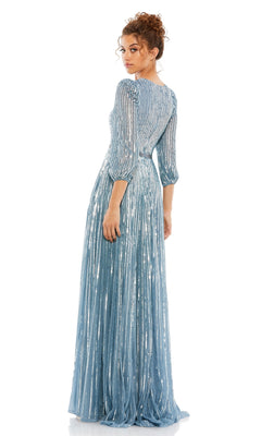 A woman in the Mac Duggal 5509 long sleeve formal dress—light blue with shimmery sequins and sheer full-length sleeves—stands and looks over her shoulder against a white background.