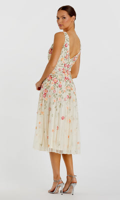 A woman models the Mac Duggal 5527 Floral-Embroidered Party Dress, a sleeveless cream tea-length dress, paired with silver high-heeled sandals, standing with her back turned and head looking over her shoulder at the camera.