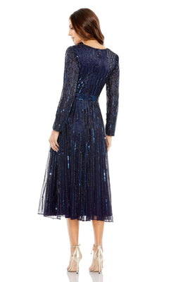A woman stands facing away in the Short Semi-Formal Dress 5528 by Mac Duggal, featuring long sleeves, navy blue sequins, an A-line tea length silhouette with a pleated skirt, paired with silver high heels.