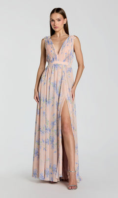 A woman wears a sleeveless, floor-length violet multi Mac Duggal 55321 evening gown with blue floral print, deep V-neckline, pleated bodice, and thigh-high slit as she stands elegantly against a plain background.
