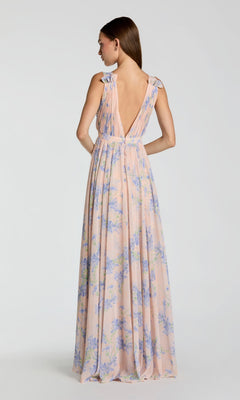 A woman wears the Mac Duggal 55321 Classic Long Formal Dress, featuring a bohemian style, deep V-back, and pastel floral print, standing against a plain light background.