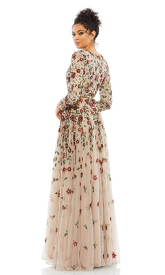 A woman poses in the Mac Duggal 5533 Beaded Long Sleeve Formal Dress, a sheer beige gown with red, pink, and green floral embroidery, against a plain white background.