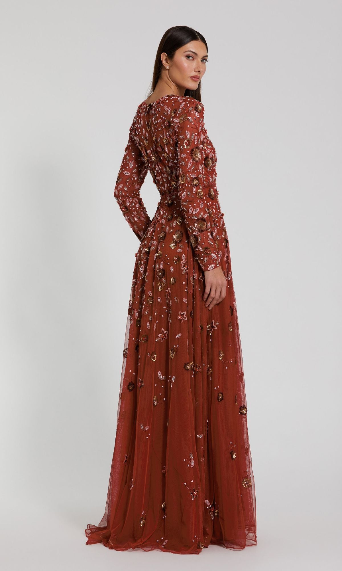 A woman wearing the Mac Duggal 5533 Beaded Long Sleeve Formal Dress stands against a plain background, looking over her shoulder.