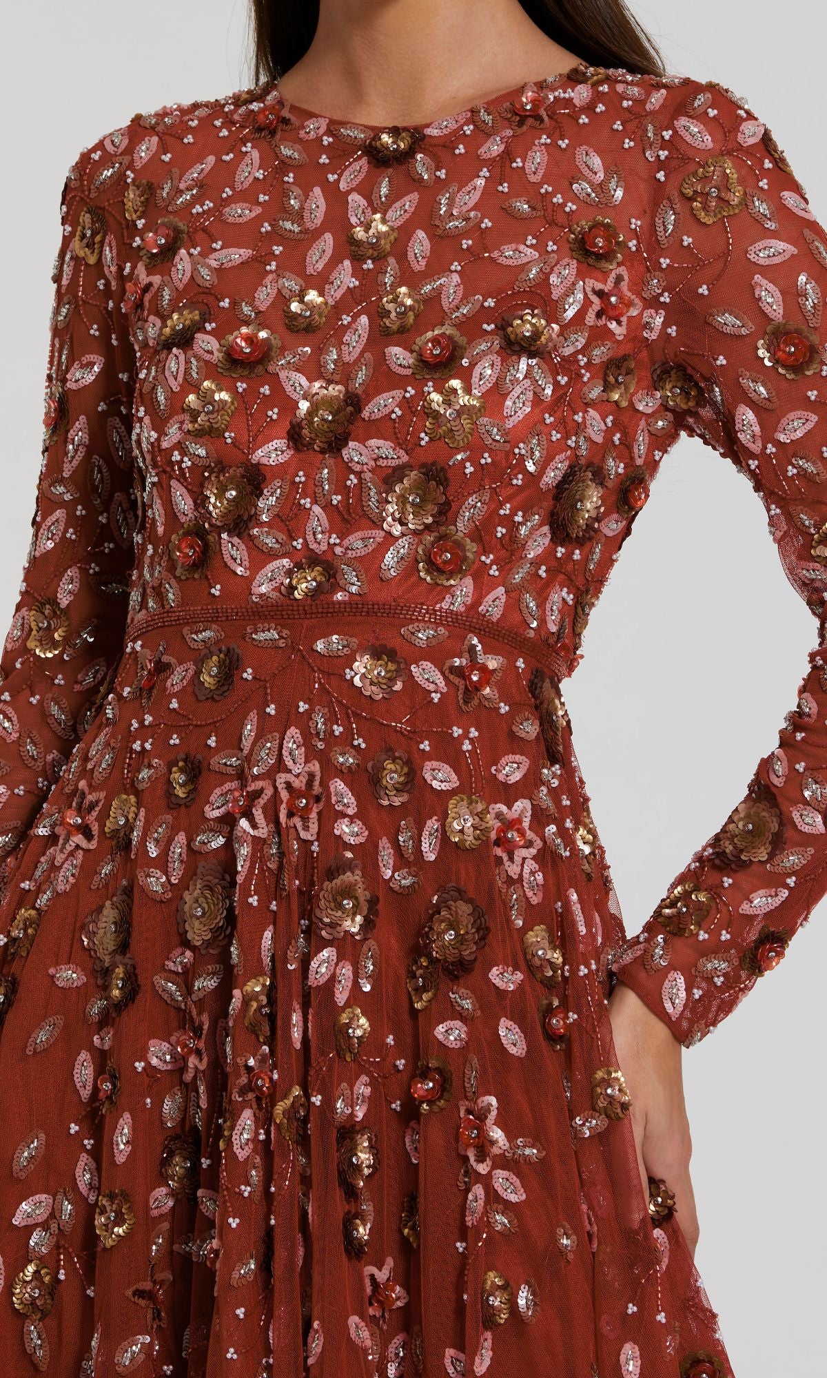 A person wearing the Mac Duggal 5533 Beaded Long Sleeve Formal Dress, a rust-colored gown featuring intricate floral embroidery and delicate beadwork.