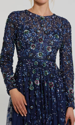 A person wearing the Mac Duggal 5533 Beaded Long Sleeve Formal Dress in navy blue, with sheer fabric, intricate floral embroidery, and beading for a stunning prom look.