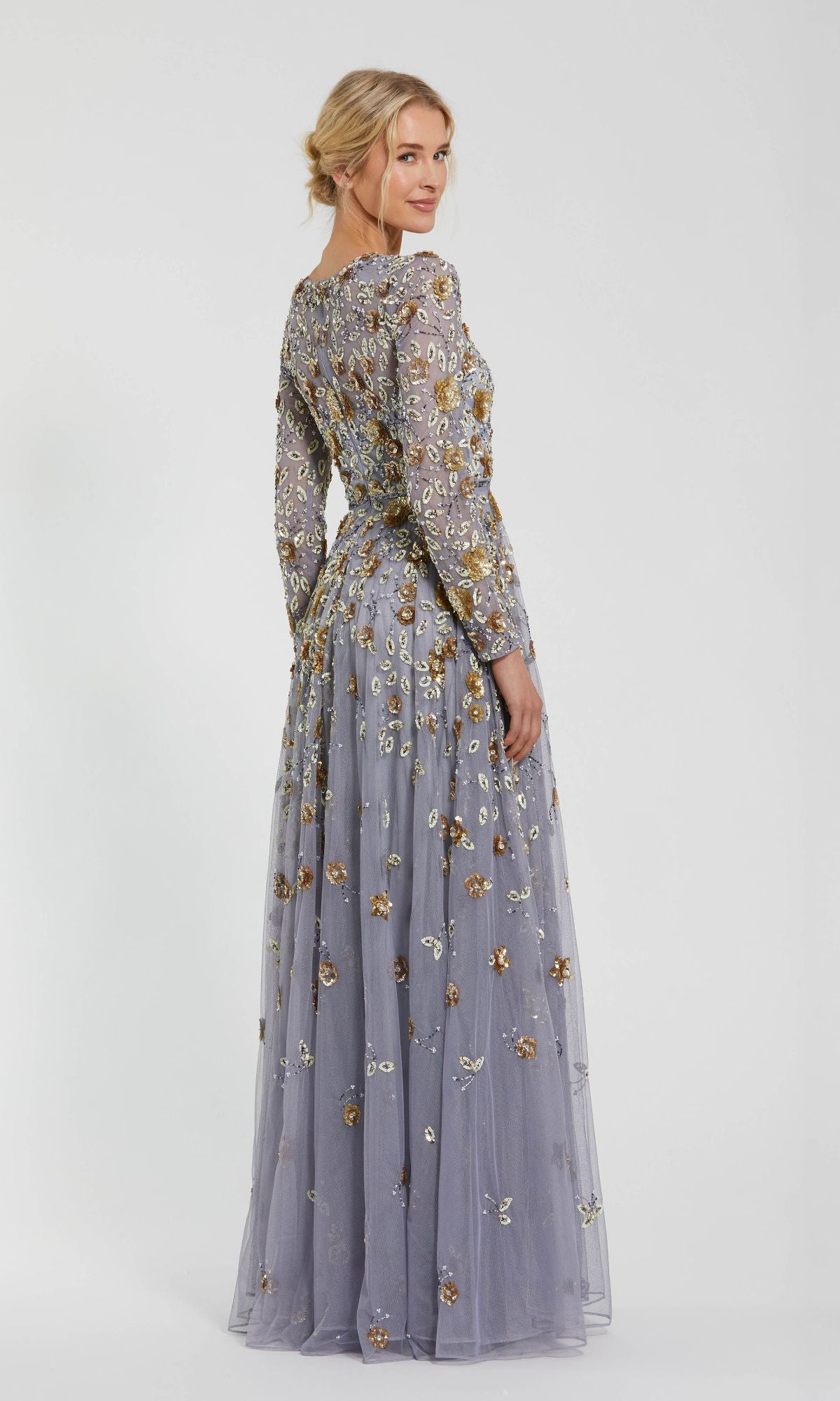A woman poses in the Mac Duggal 5533 Beaded Long Sleeve Formal Dress—a floor-length lavender gown with floral embroidery—glancing over her shoulder against a plain white background.
