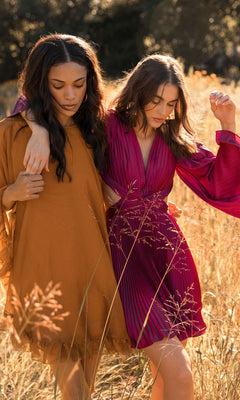 Two women stroll through a sunlit field: one in a mustard yellow dress, the other in the Mac Duggal 55407 Cape-Sleeve Short Ruffled Party Dress—both exuding semi-formal cocktail style.