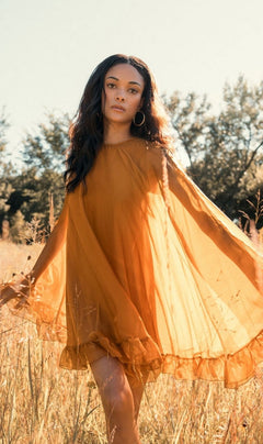 A person stands in a field under daylight, wearing the Mac Duggal 55407 Cape-Sleeve Short Ruffled Party Dress, surrounded by tall grass and trees. The scene highlights the dress's semi-formal elegance in a natural outdoor setting.