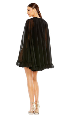 A woman stands in profile wearing the Mac Duggal 55407 Cape-Sleeve Short Ruffled Party Dress with a sheer black overlay and metallic heels—ideal as a semi-formal cocktail option—against a white background.