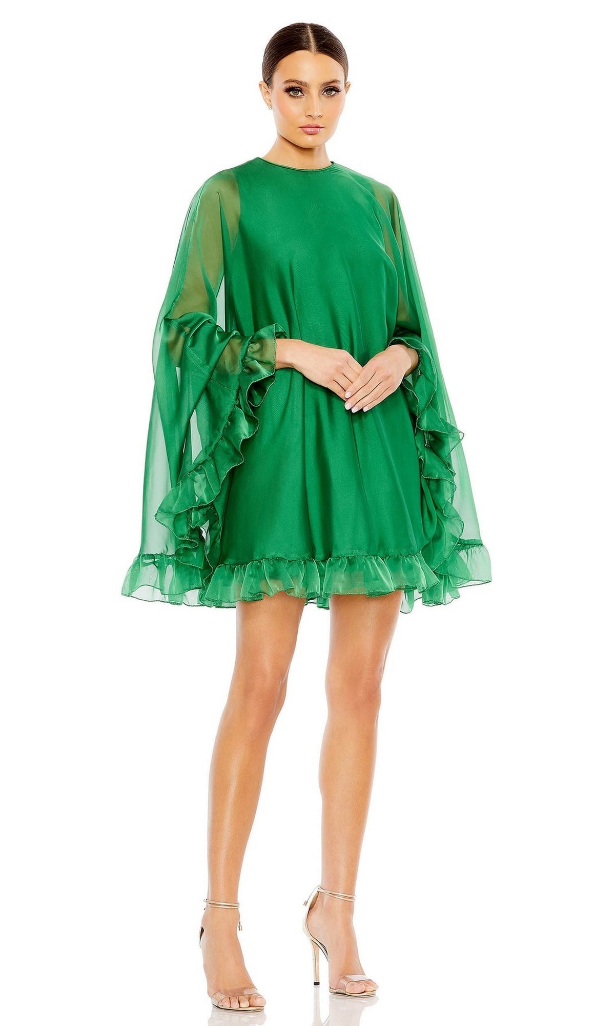 A woman in the Mac Duggal 55407 Cape-Sleeve Short Ruffled Party Dress with sheer sleeves and ruffled hem pairs it with silver high-heeled sandals, creating a chic semi-formal cocktail look against a white background.