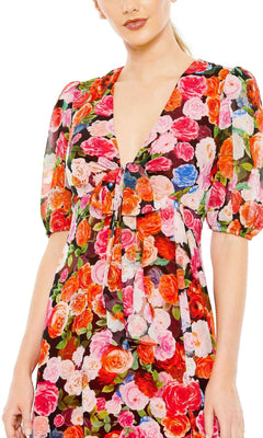 A woman wears the Mac Duggal 55626 Short Sleeve Midi Print Party Dress, featuring a deep V-neckline and a vibrant red, pink, orange, and blue floral pattern.