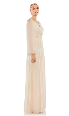 A woman models the Mac Duggal 55694, a long sleeve chiffon formal dress with decorative shoulders, in light beige against a plain white background, presenting an elegant mother of the bride look.