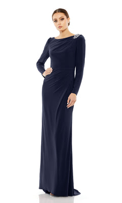 A woman models the Long Formal Dress 55695 by Mac Duggal in navy, featuring a fitted silhouette with subtle draping and striking shoulder embellishments, posed against a white background.