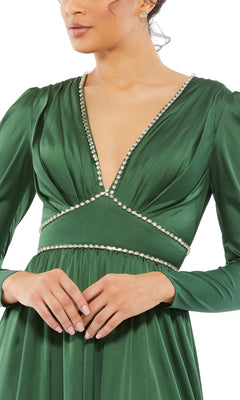 A woman wears the Long Formal Dress 55702 by Mac Duggal, a deep green gown with long sleeves, a v-neckline, and sparkling rhinestone trim accenting the neckline and waist.