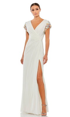A woman stands in silver heels, wearing the Cap-Sleeve Long Formal Gown: Mac Duggal 55709, a white dress with a slit, V-neckline, and colorful embellished cap sleeves.