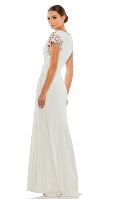 Woman in a white Mac Duggal 55709 Cap-Sleeve Long Formal Gown, featuring floral embroidery, stands and looks over her shoulder against a white background.