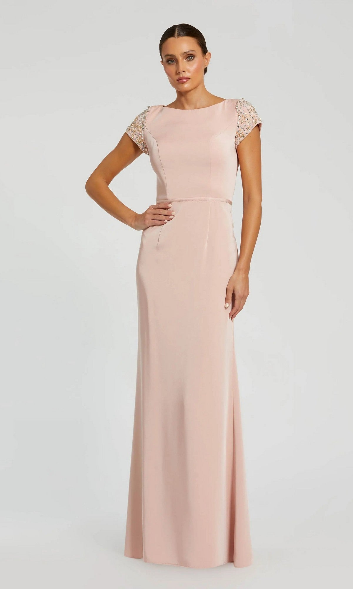 A woman models the Long Formal Dress 55718 by Mac Duggal, featuring a blush pink hue, cap sleeves with embellishments, and a floor-length silhouette against a simple light background.