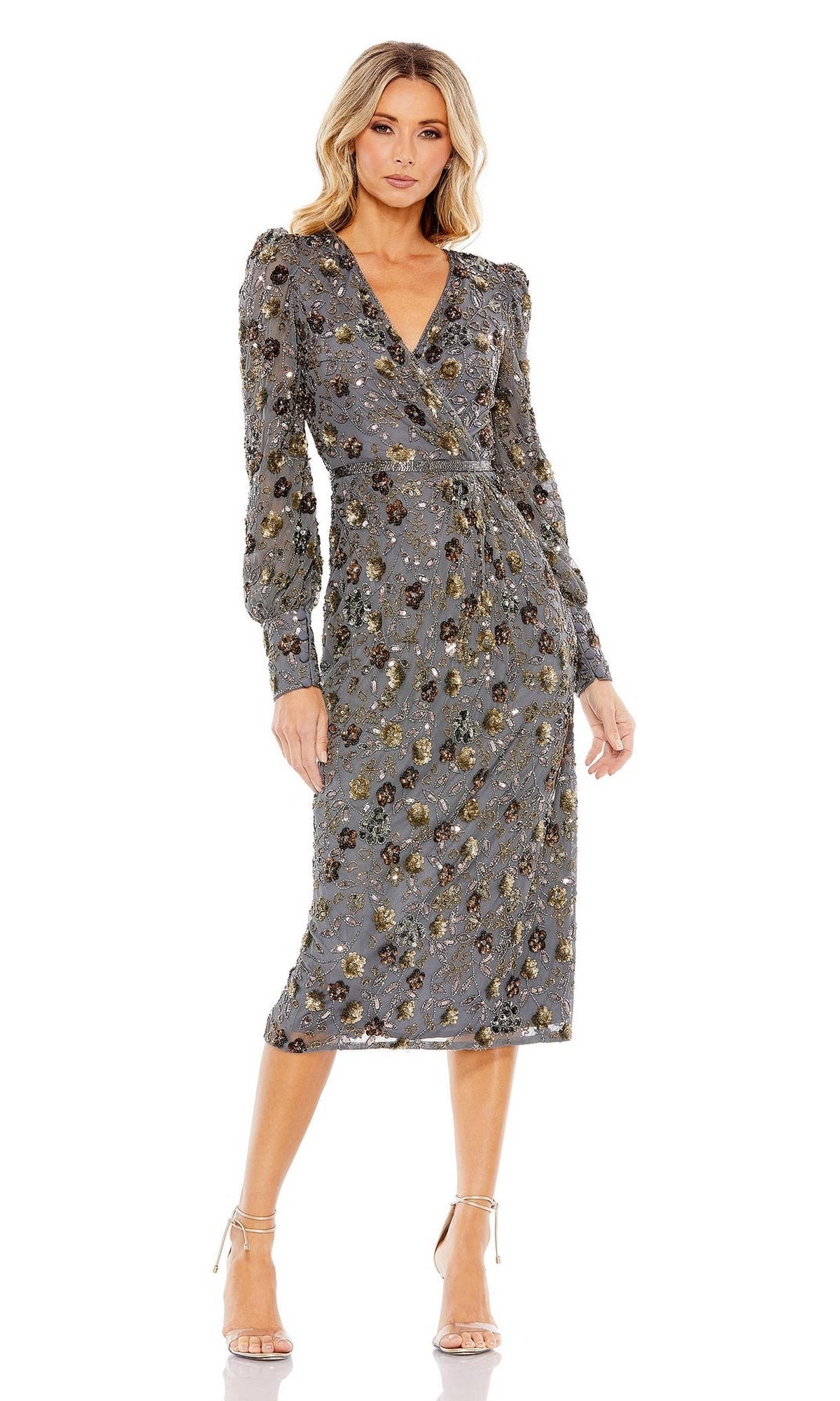 A woman wears the Short Semi-Formal Dress 5571 by Mac Duggal, a charcoal beaded, long-sleeve, knee-length dress with floral patterns and gold accents, paired with beige high-heeled sandals.