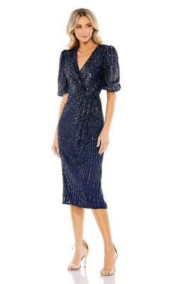 A woman wearing the Mac Duggal Short Semi-Formal Dress 5578—midnight blue, knee-length, with a v-neckline, puff sleeves, and silver sequins—paired with silver high-heeled sandals.