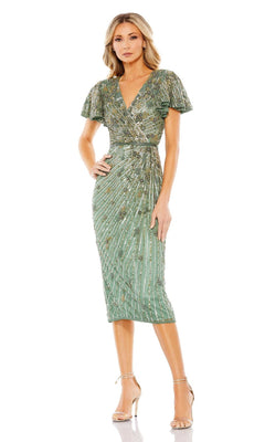 A woman wears the Mac Duggal 5582 Midi Sage Green Semi-Formal Dress, featuring a fitted knee-length silhouette, short sleeves, V-neck, draped details, and metallic accents. She pairs it with high-heeled sandals against a white background.