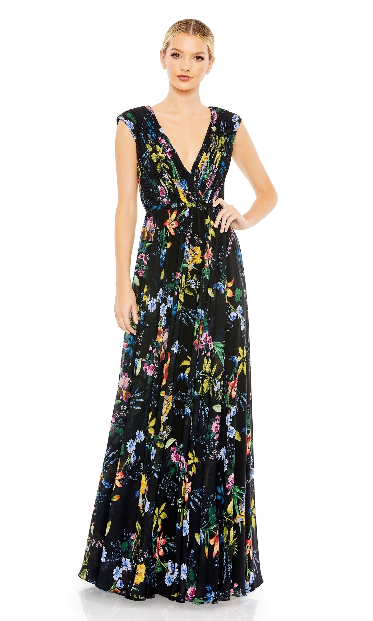 A woman stands against a white background wearing the Mac Duggal 55829 Long Floral-Print Formal Dress, a sleeveless formal gown with a deep V-neckline and colorful floral pattern.