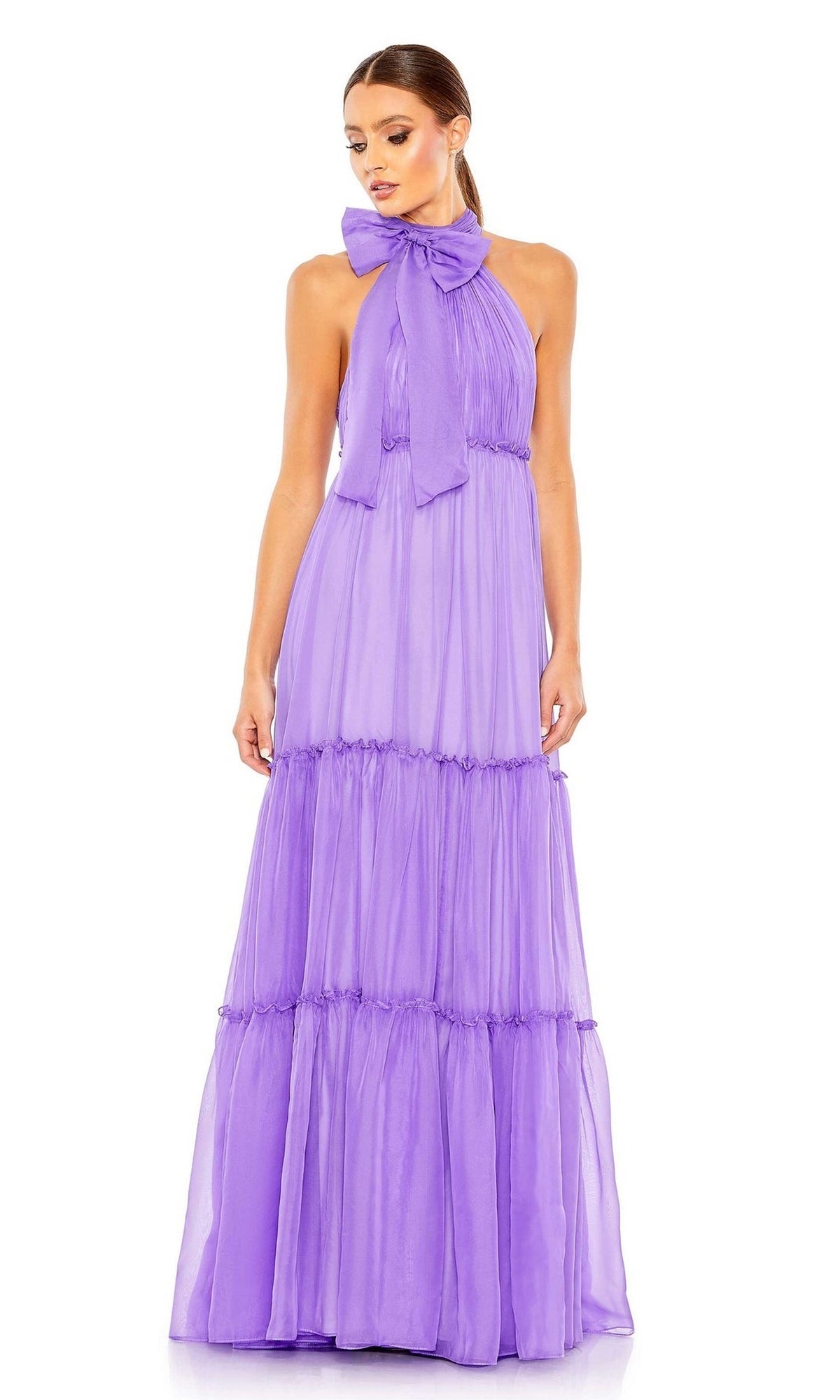 A woman wears the High-Neck Long Formal Dress: Mac Duggal 55848—a floor-length lavender gown with a large neck bow and tiered ruffled skirt, ideal for any glamorous event.