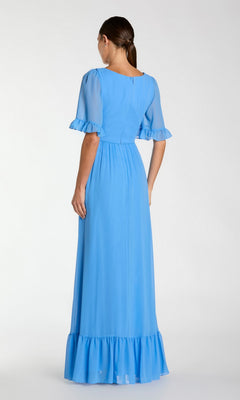 A woman stands with her back to the camera, wearing the Long Formal Dress 55867 by Mac Duggal— a light blue, short-sleeve, floor-length A-line dress with ruffle details on the sleeves and hem.