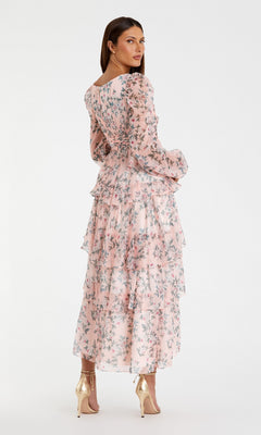 A woman models the Mac Duggal 55880 Print Midi Wedding Guest Dress with long sleeves and floral print, paired with gold heels, facing away with her head turned—an ideal chic choice for a wedding guest.