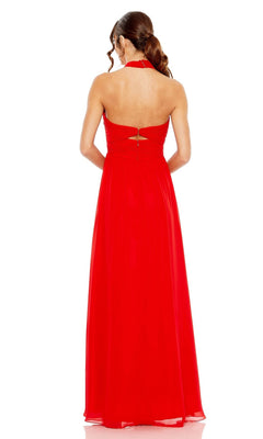 A woman stands against a white background wearing the Mac Duggal Long Formal Dress 55898, a floor-length, sleeveless red ruched halter neck gown with an open back and loose waves in her hair.