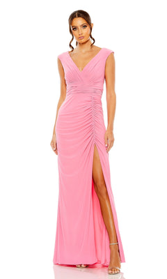 A woman wears the Long Formal Dress 55974 by Mac Duggal, a candy pink V-neck gown with a ruched bodice, high slit, and strappy heels—an elegant formal look set against a white background.