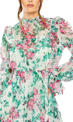 A woman wears the High-Neck Print Party Dress 56008 by Mac Duggal, featuring long sleeves and a pink and green floral print on sheer, lightweight fabric.