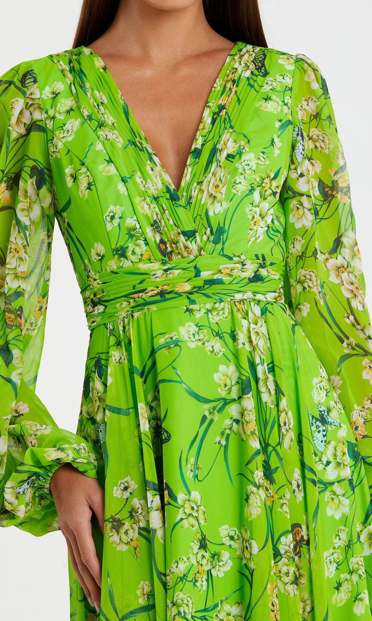 A woman wears the Long Green Print Formal Dress: Mac Duggal 56013, featuring a bright green floral print, long sleeves, and a V-neckline; her left hand rests on her hip.