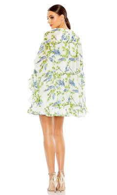 Woman in high heels wears the Cape Short Party Dress 56029 by Mac Duggal—white with green and blue floral patterns, loose fit, shown from the back.