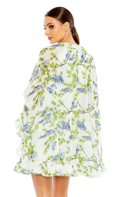 A woman with brown hair in a low ponytail is seen from the back wearing the Mac Duggal Cape Short Party Dress 56029, a loose white dress with blue and green floral designs.