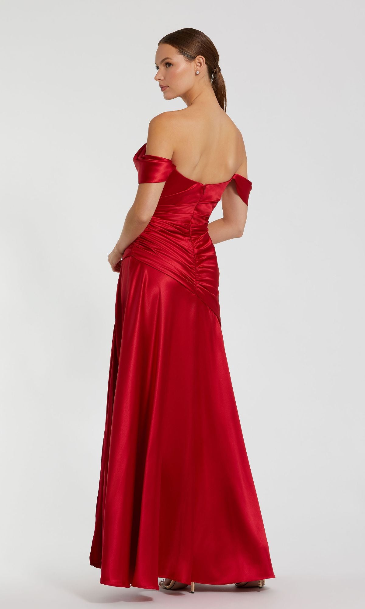 A woman faces away from the camera in the elegant Mac Duggal 56037, an off-the-shoulder, floor-length red satin prom dress, shown against a plain light background.