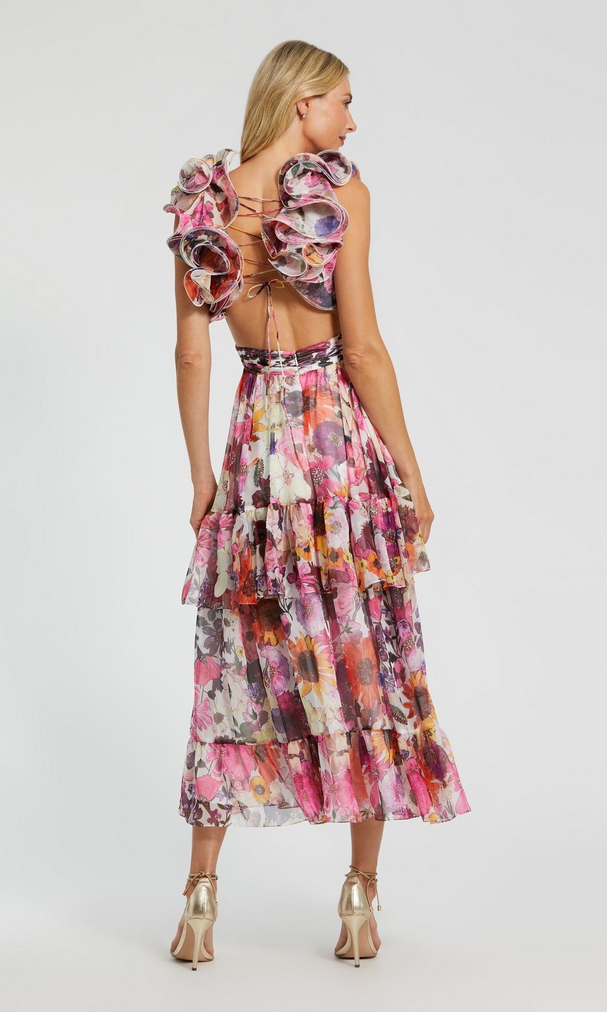 A woman faces away, wearing the Midi Wedding Guest Dress: Mac Duggal 56048 featuring a floral print, ruffled shoulders, lace-up open back, and metallic high heels.