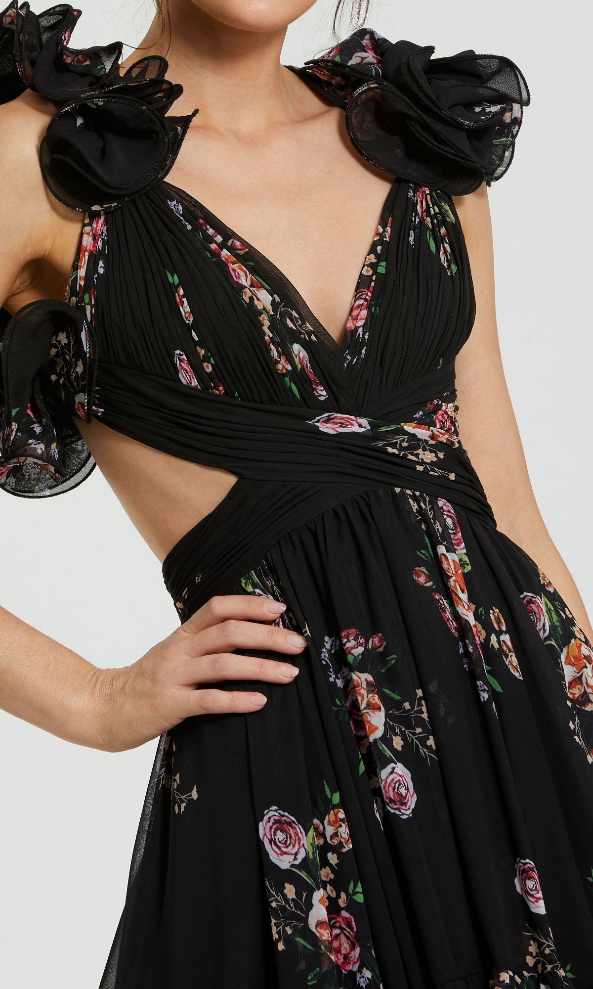 A person wearing the Mac Duggal 56054 Cut-Out Black Print Formal Dress, featuring floral prints, ruffled shoulder details, a deep V-neckline, and stylish cut-out sides—an elegant evening gown.