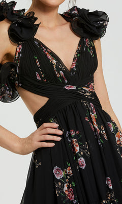 A person wearing the Mac Duggal 56054 Cut-Out Black Print Formal Dress, featuring floral prints, ruffled shoulder details, a deep V-neckline, and stylish cut-out sides—an elegant evening gown.