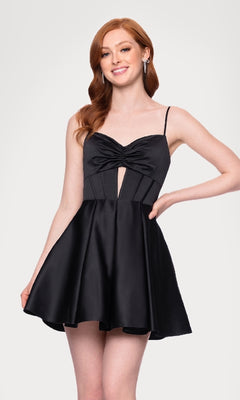 Woman with long red hair wears the Cut-Out Black Mini Hoco Dress (Blondie Nites 5605BN), a sleeveless black homecoming dress with thin straps and front knot detail, against a plain light background.
