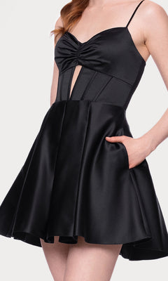 A woman wears the Cut-Out Black Mini Hoco Dress: Blondie Nites 5605BN—an a-line black satin party dress with thin straps, fitted bodice and front cut-out, flared skirt, and side pocket—perfect as a chic homecoming look.
