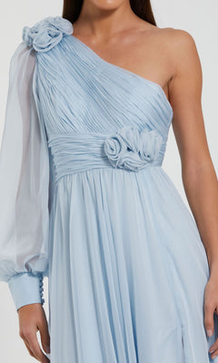 A woman wears the Mac Duggal 56070 Light Blue Long Formal Dress featuring a one-shoulder design, pleated fabric, floral accents, and a sheer long sleeve with buttoned cuff—perfect for special occasions.