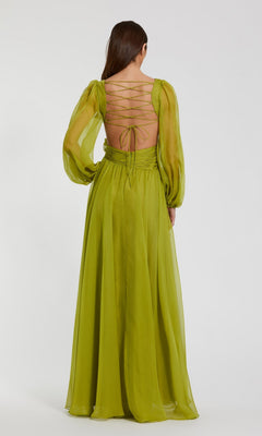 A woman with long brown hair wears the Mac Duggal 56072, a floor-length light green chiffon formal dress featuring sheer long bishop sleeves and an open back with lace-up detailing.