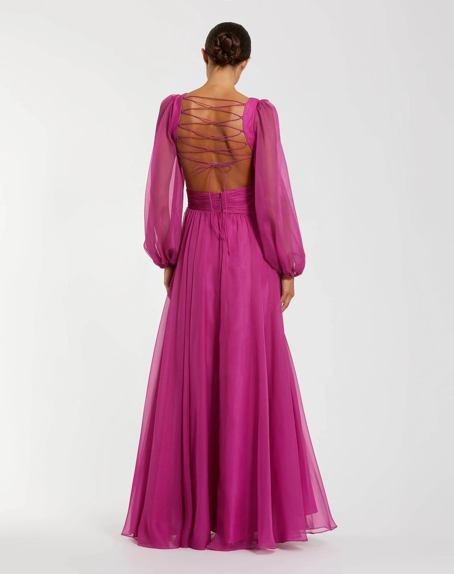 A person is wearing the Long Formal Dress, Mac Duggal 56072—a magenta chiffon evening gown with sheer long bishop sleeves and an open back featuring crisscross lace-up detailing—while standing against a plain white background.