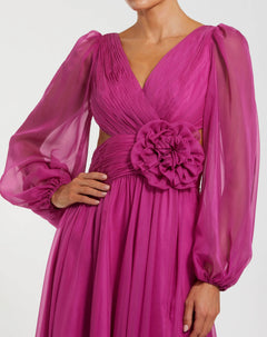 Wearing the Mac Duggal 56072 Long Formal Dress in magenta chiffon, which features sheer long bishop sleeves, a pleated bodice, a cut-out waist, and a statement fabric flower at the center.